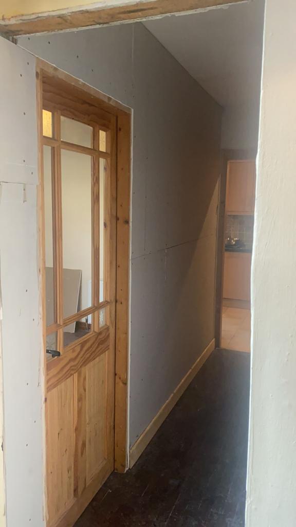 Wooden doorway with glass panels, leading to a hallway with dark flooring and gray walls.