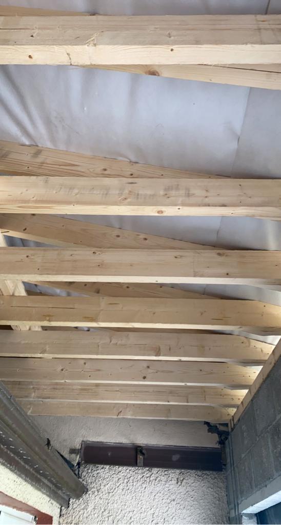 Wooden beams forming a ceiling structure, with white material above.