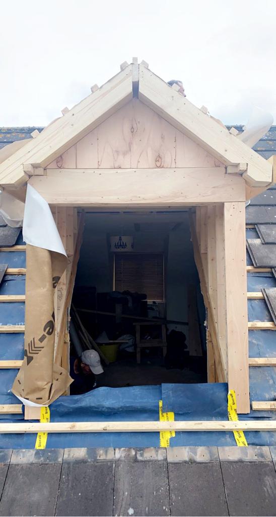 Wooden dormer window frame under construction on a tiled roof.
