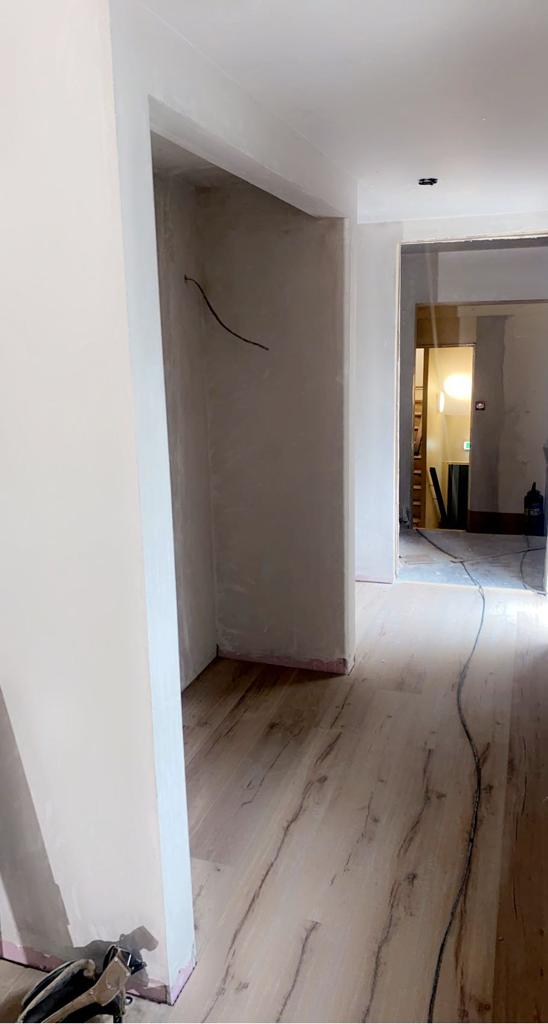 Hallway with unfinished walls, light wood flooring, and exposed wiring.