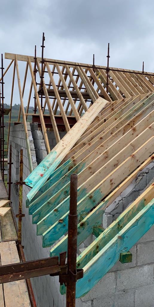 Roof construction in progress with wooden rafters and scaffolding. Cloudy sky overhead.