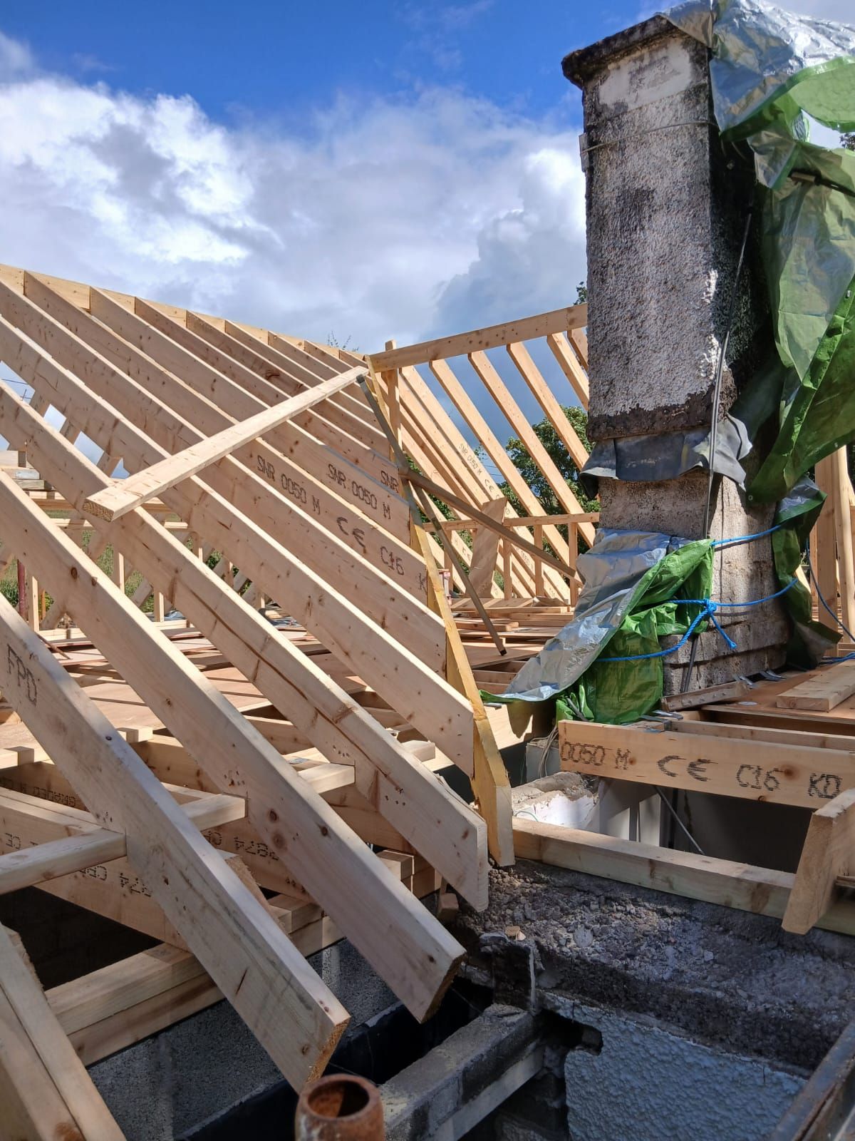 Wooden roof frame under construction with a chimney and cloudy sky.