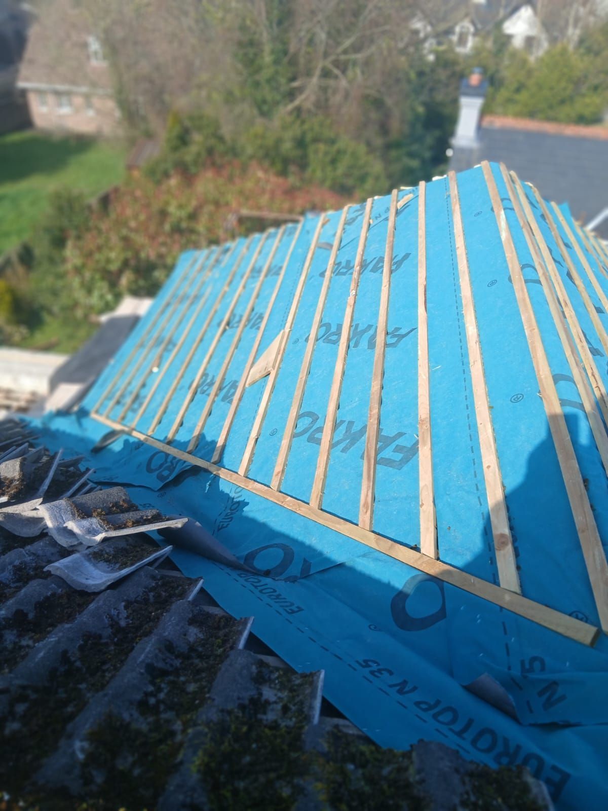 Roof under construction; blue roofing felt and wooden battens on a small peaked section.