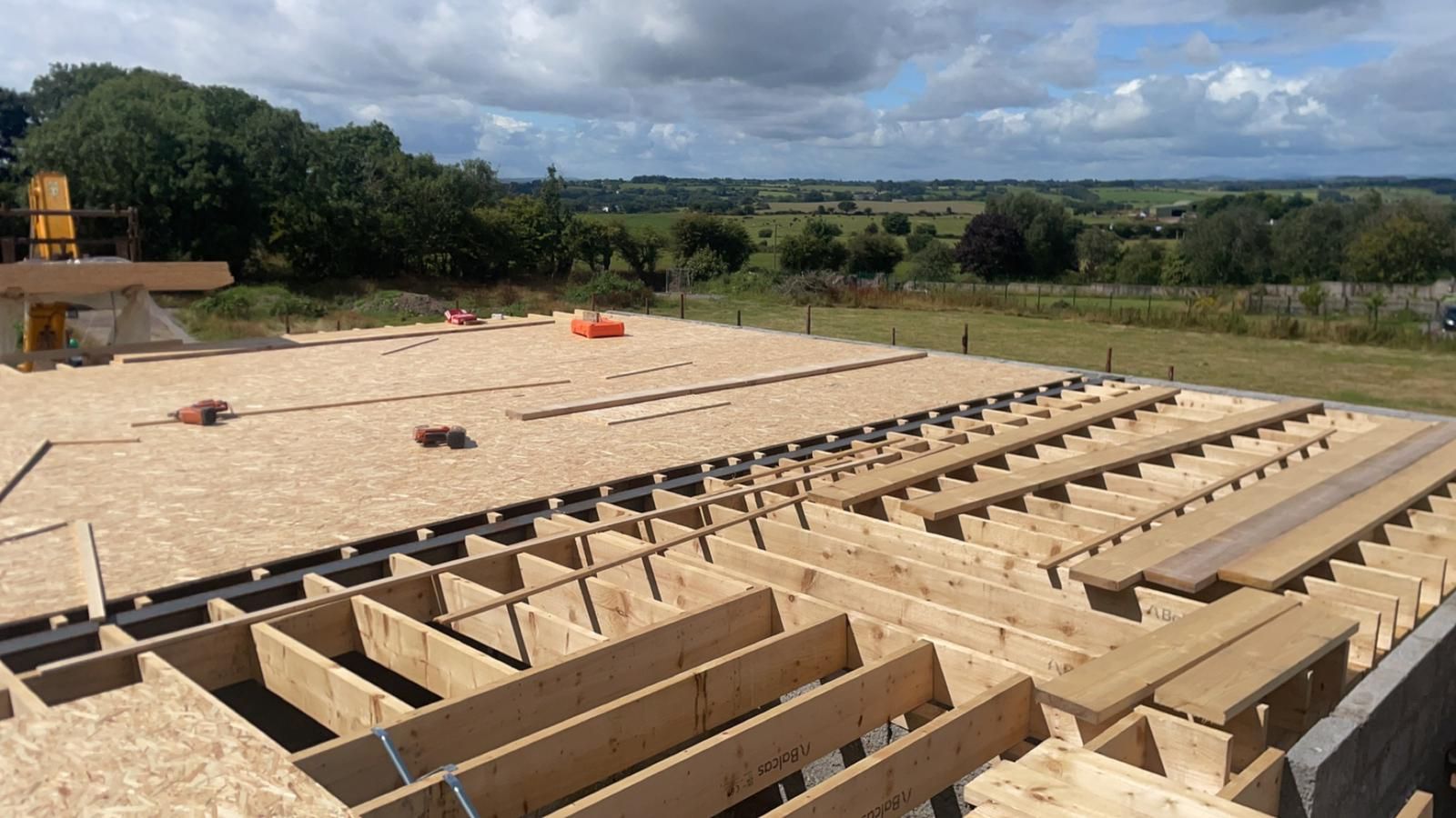 Construction site: wooden floor framing with OSB sheathing, open-air view.