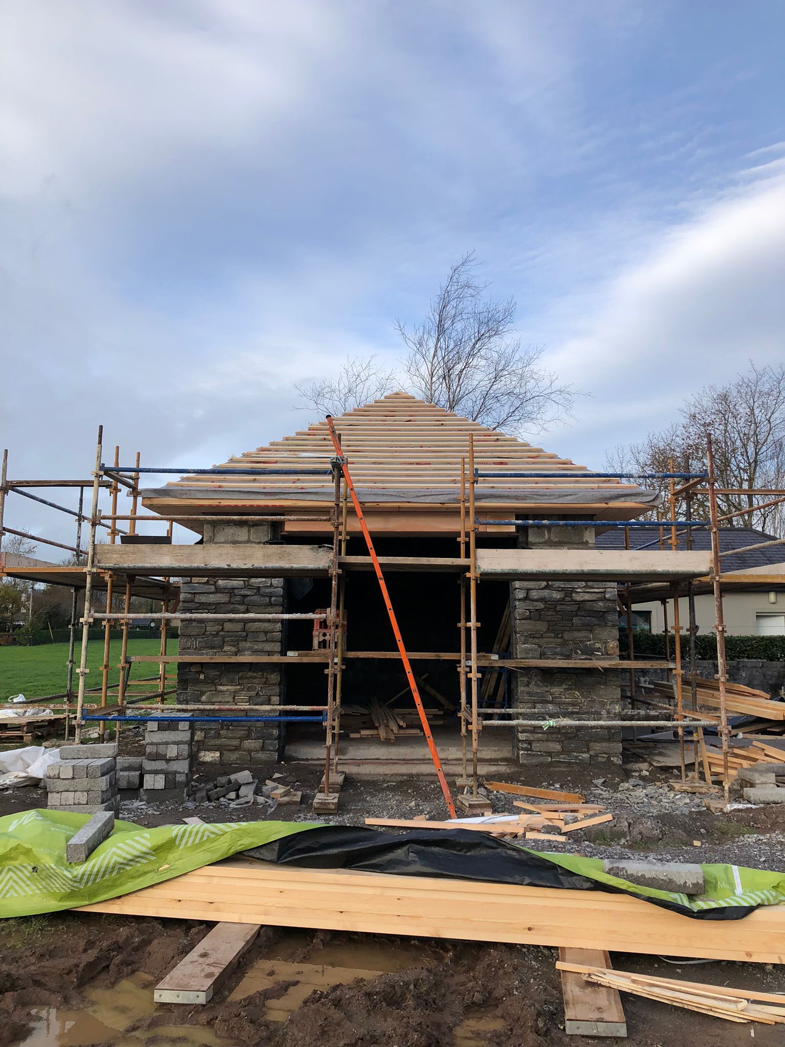 Stone building under construction with scaffolding and exposed roof framing.