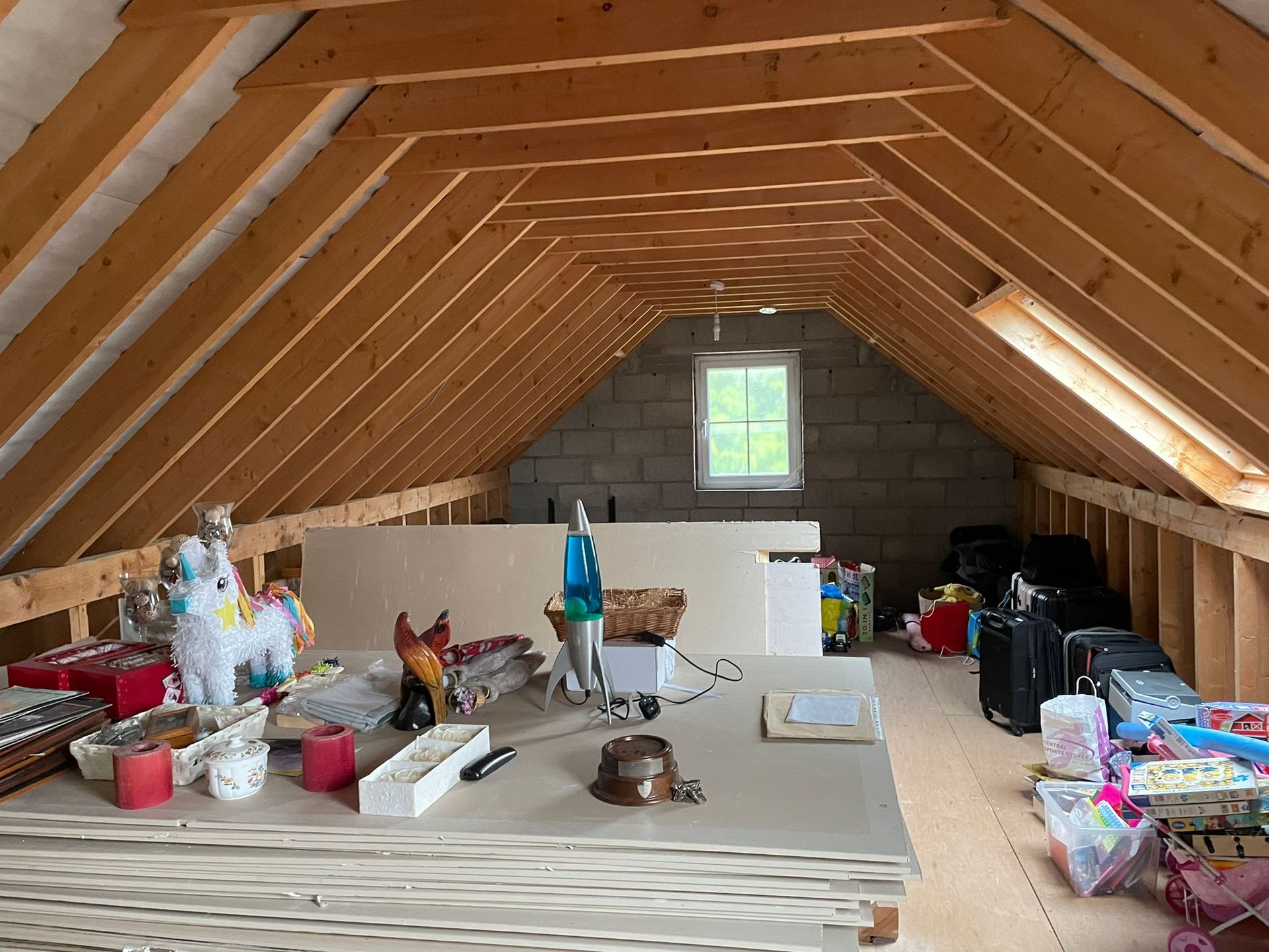 Unfinished attic with exposed wooden rafters and various stored items.