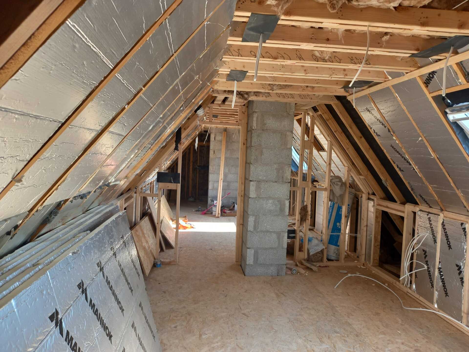 Interior of an unfinished attic space, showing exposed wood framing, insulation, and a central chimney.