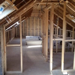 Interior framing of an attic, with wood studs and rafters. Drywall stacked in the background.