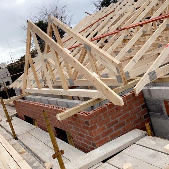 Wooden roof trusses being installed on a brick wall, part of a new construction project.