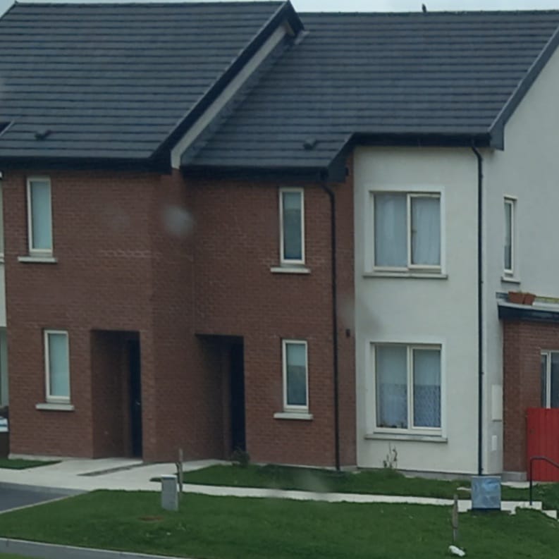 Two-story brick and white townhouse with dark gray roof, windows, and small front yards.