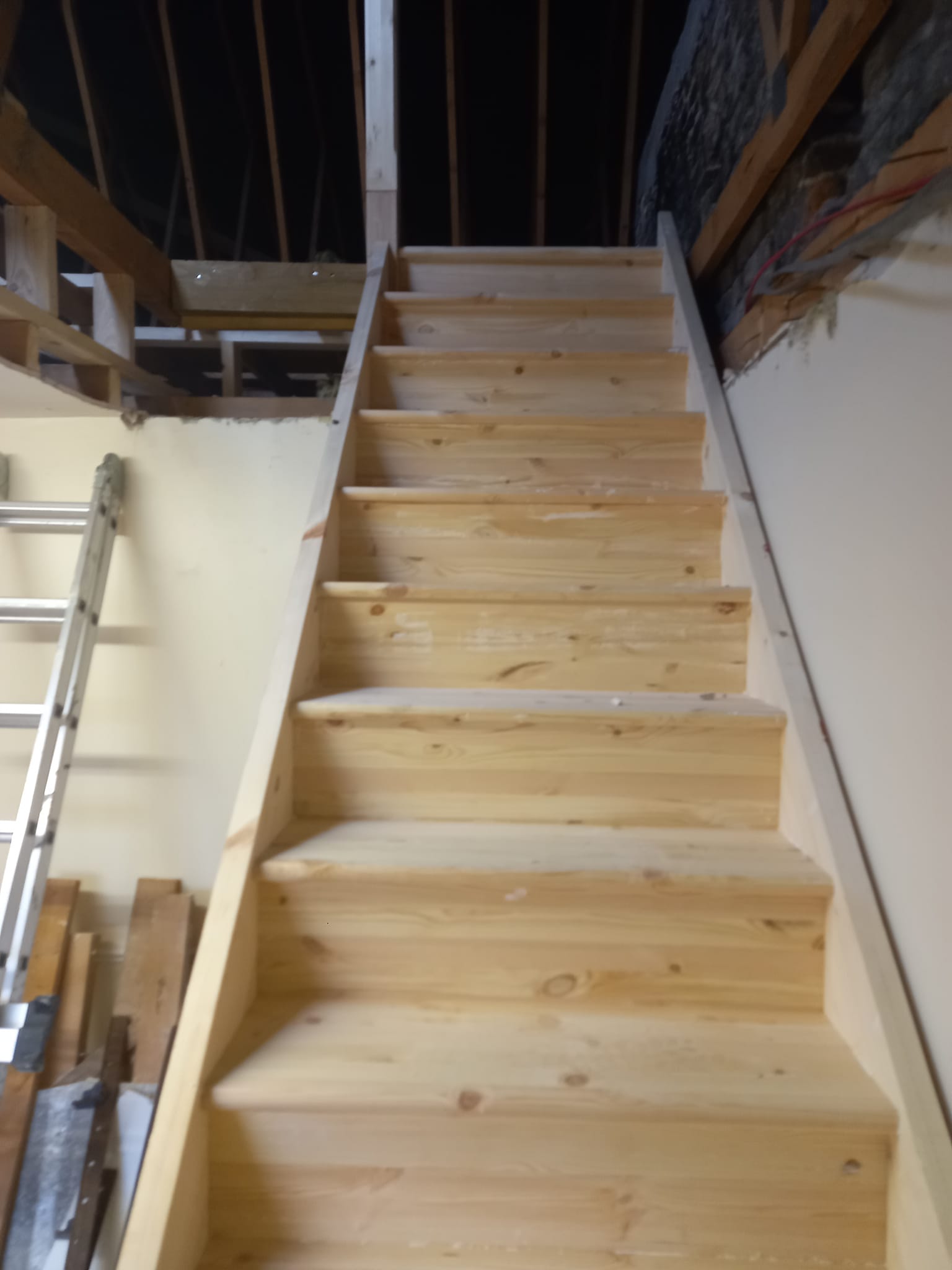 Wooden staircase leading upwards to a partially unfinished attic space.