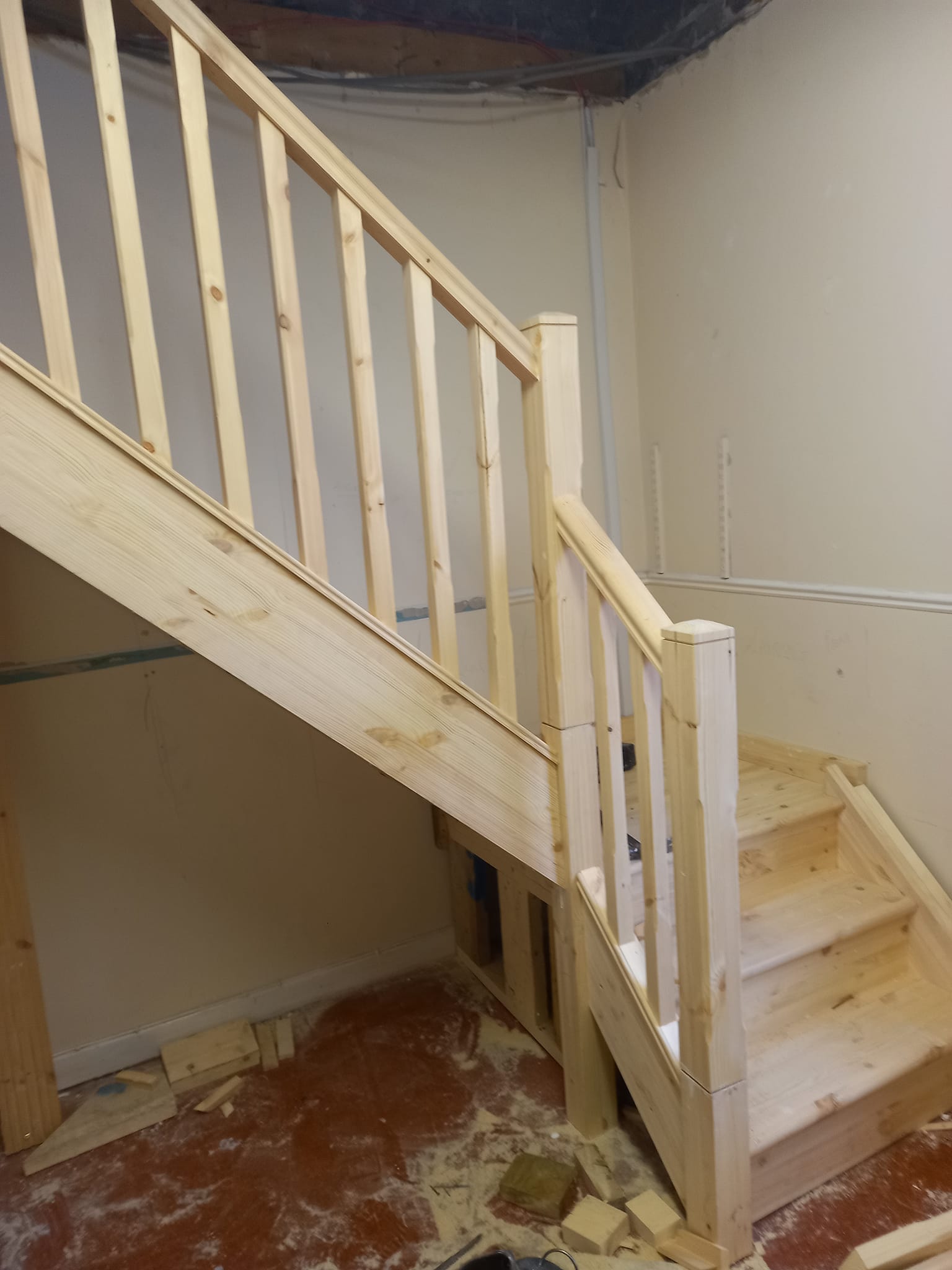 Wooden staircase with railing and unfinished steps in a room with light walls.