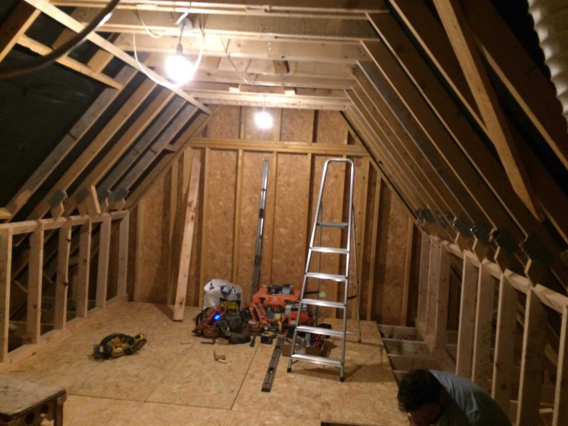 Interior framing of an attic room under construction; a ladder and tools are present.