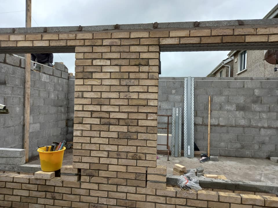 Brick and cinder block construction of a building exterior, with openings for windows or doors, under overcast skies.