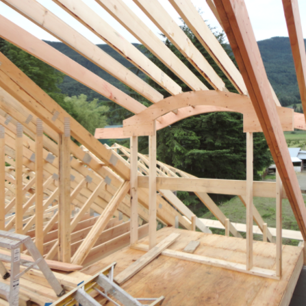 Interior view of a building under construction, showing wooden framing for walls and roof, with a curved archway.