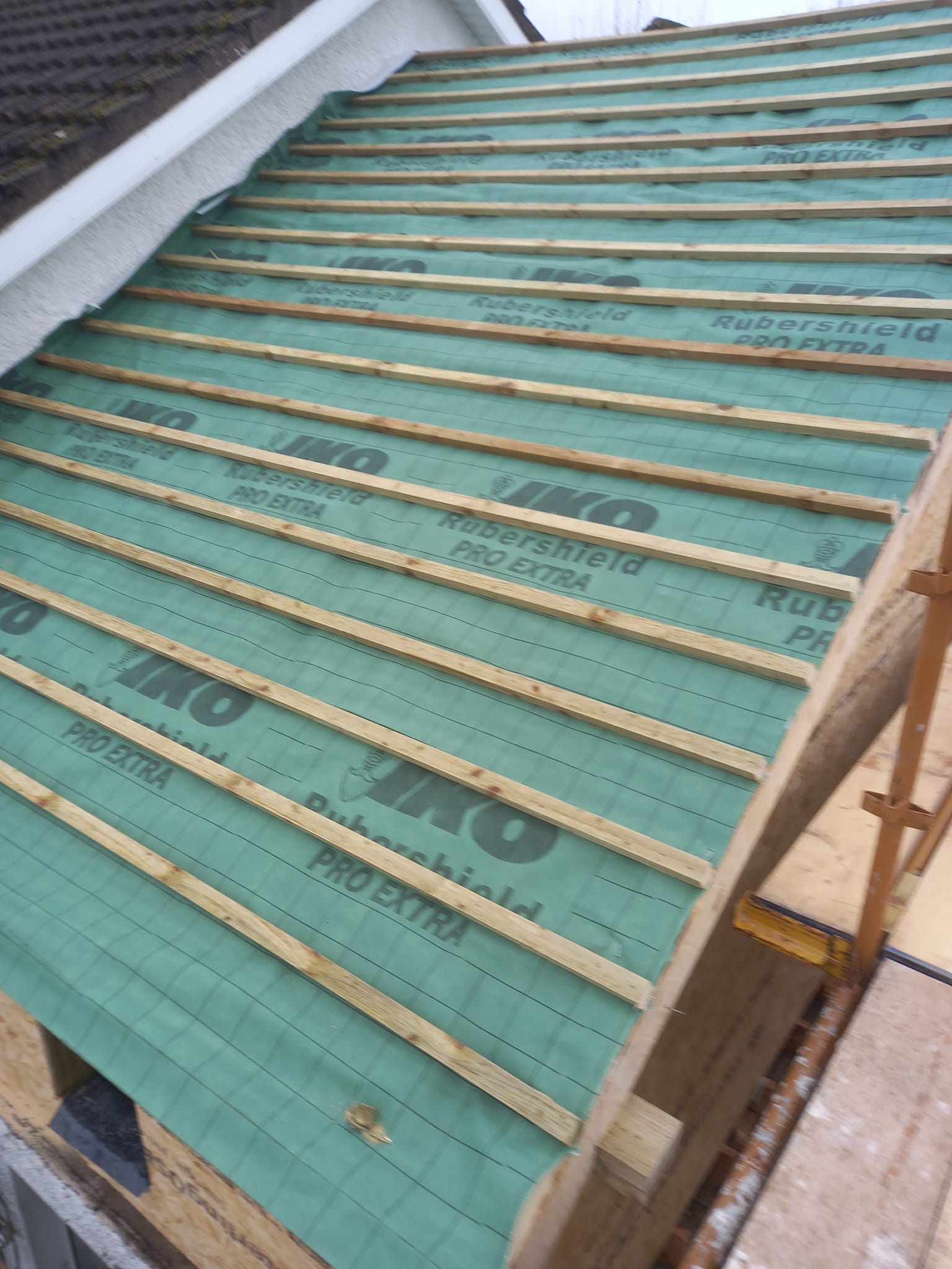 Green roofing underlayment with wood battens on a partially constructed roof.