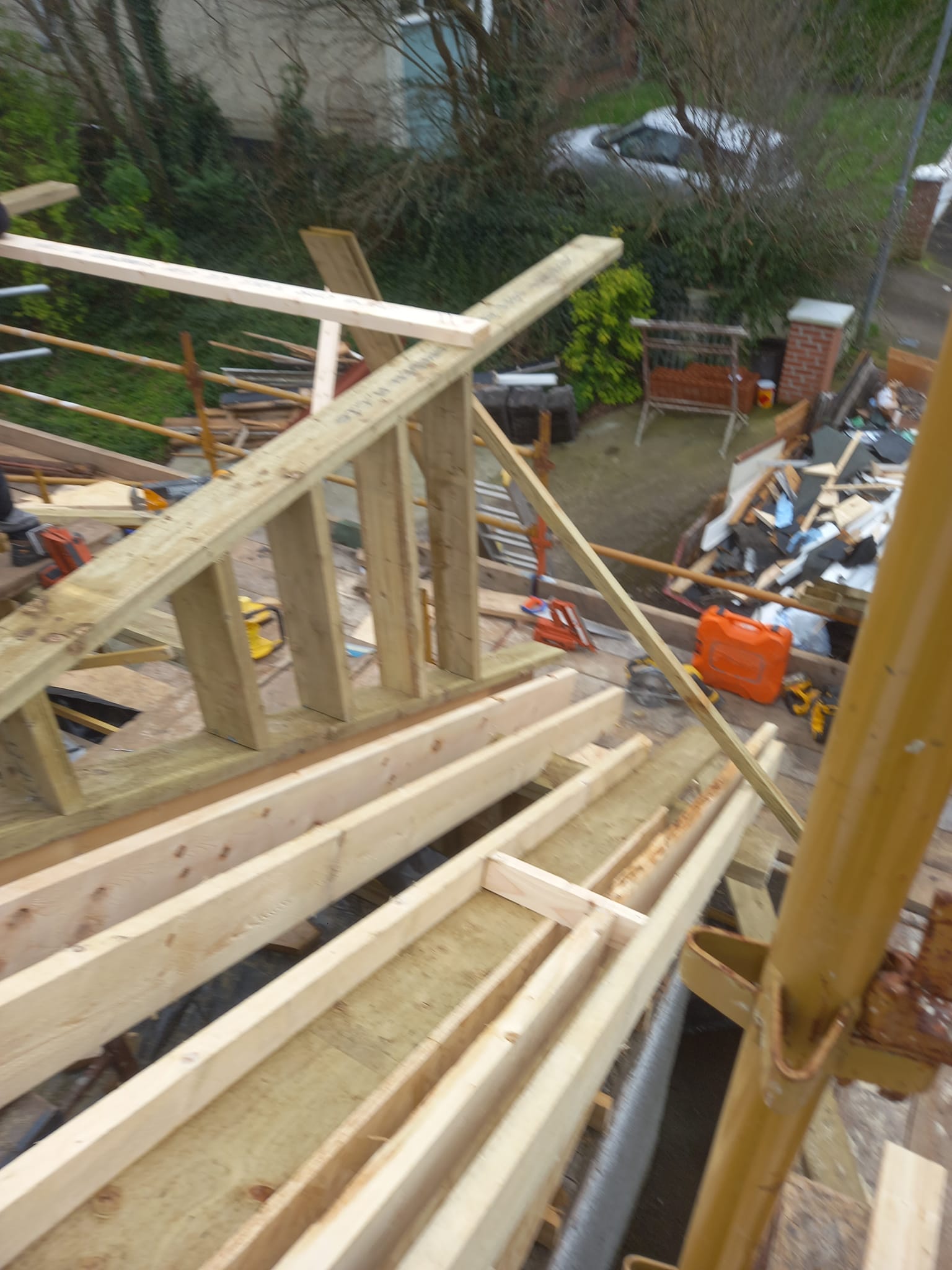 Wooden beams and scaffolding being built on a rooftop. A person may be working.