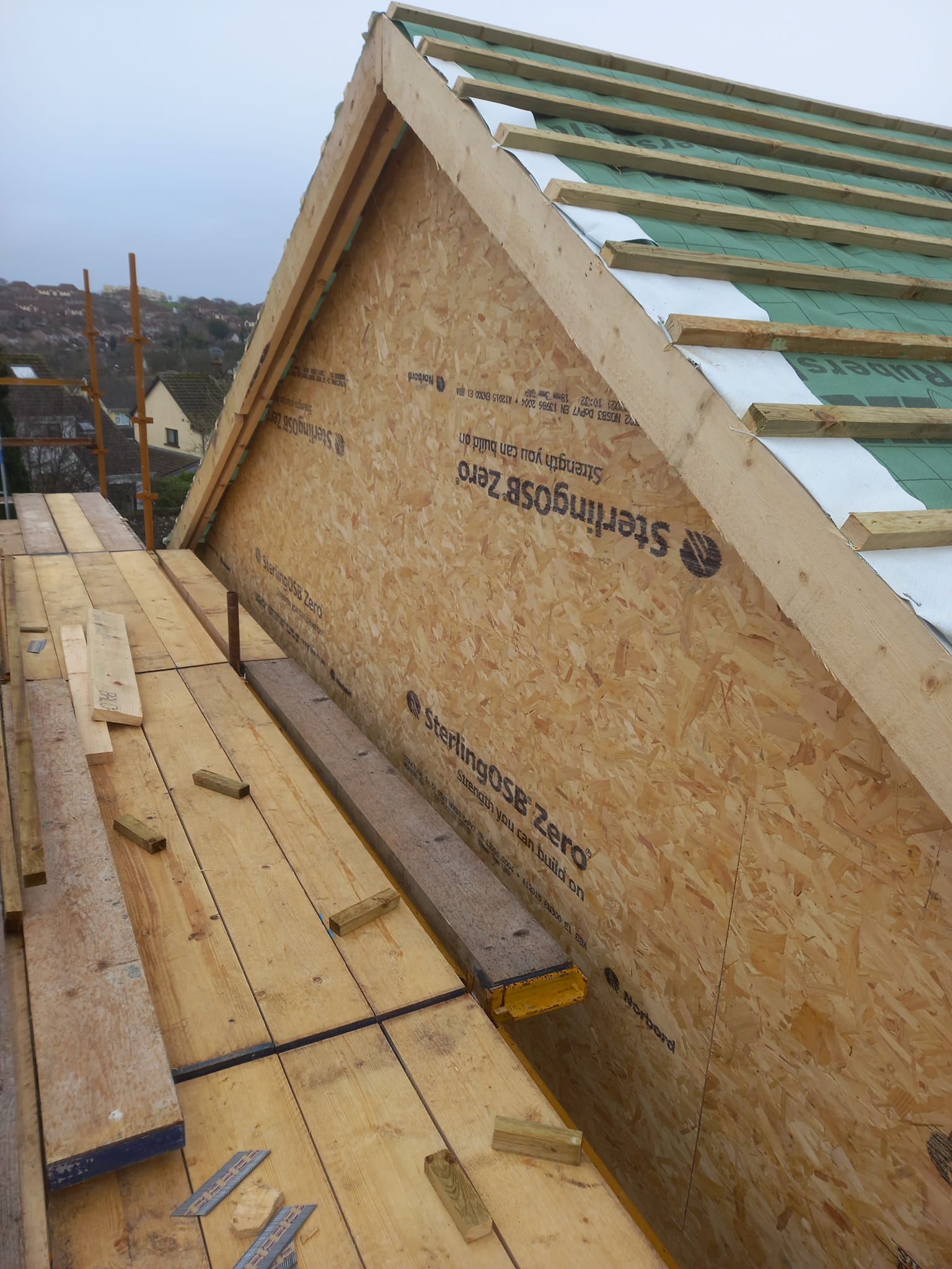 Construction of a roof. OSB sheathing on a gable end, wooden rafters, insulation, and scaffolding.