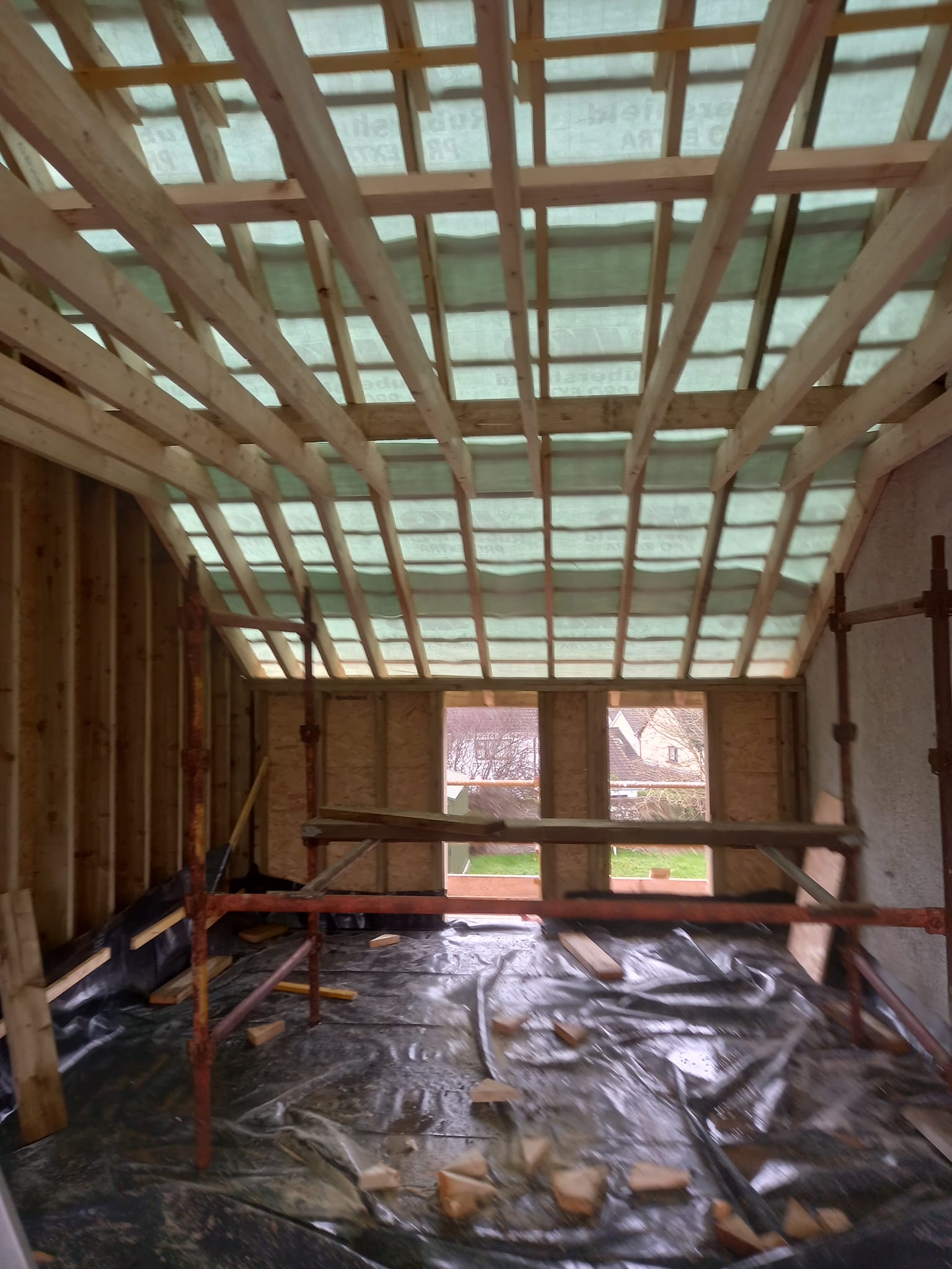 Interior view of a building under construction, showing wooden framing, scaffolding, and green tarp.