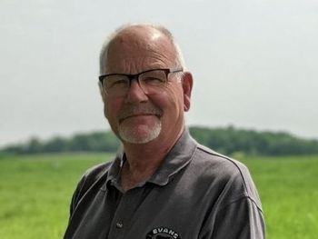 A man wearing glasses and a grey shirt is standing in a field.