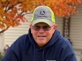 A man wearing a hat and glasses is standing in front of a house.