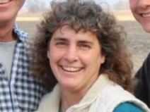 A woman with curly hair is smiling for a picture with two men.