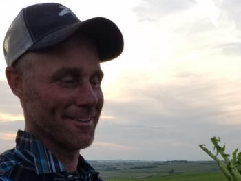 A man wearing a hat is smiling in a field