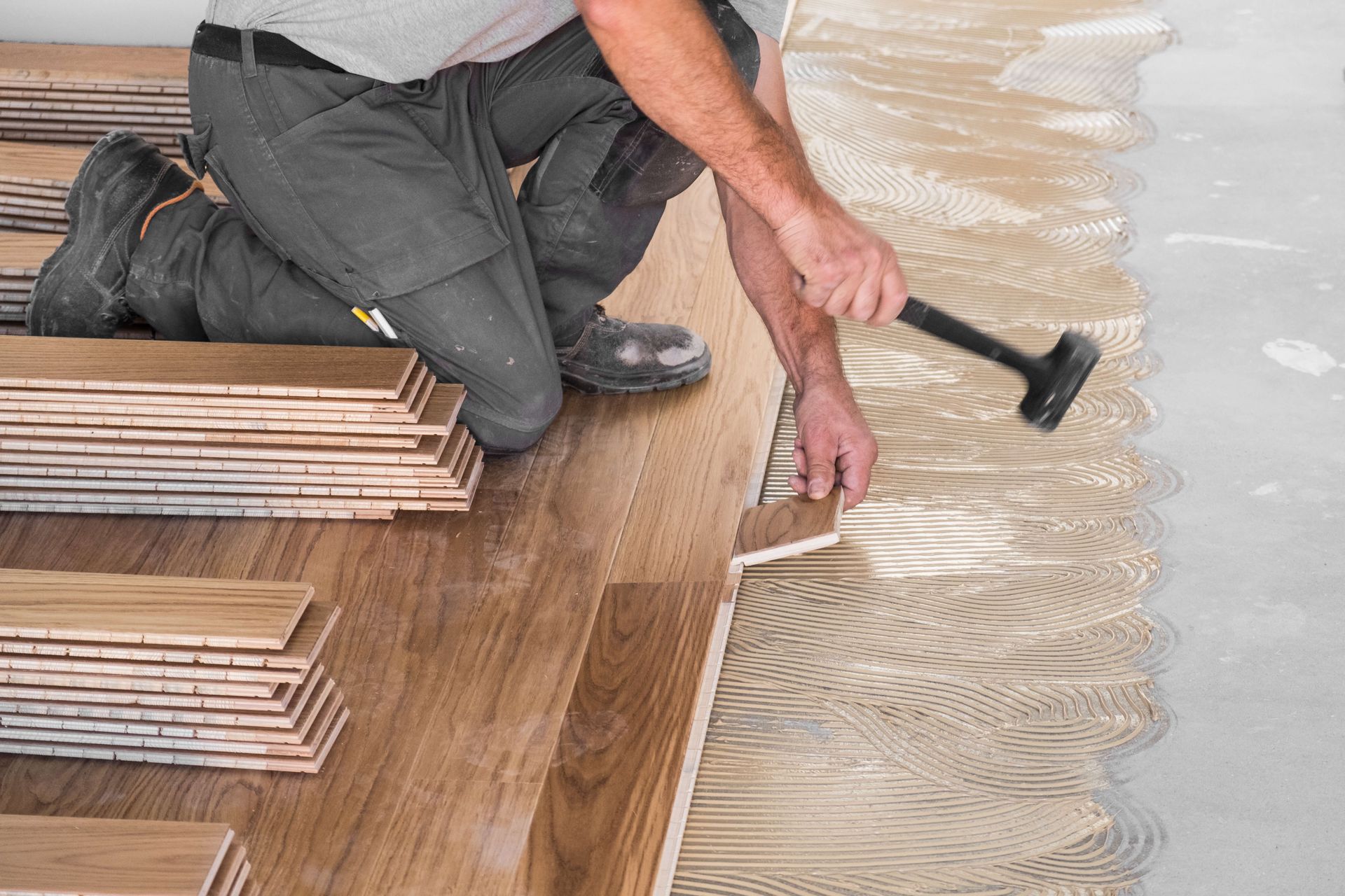 A man is installing a wooden floor with a hammer.