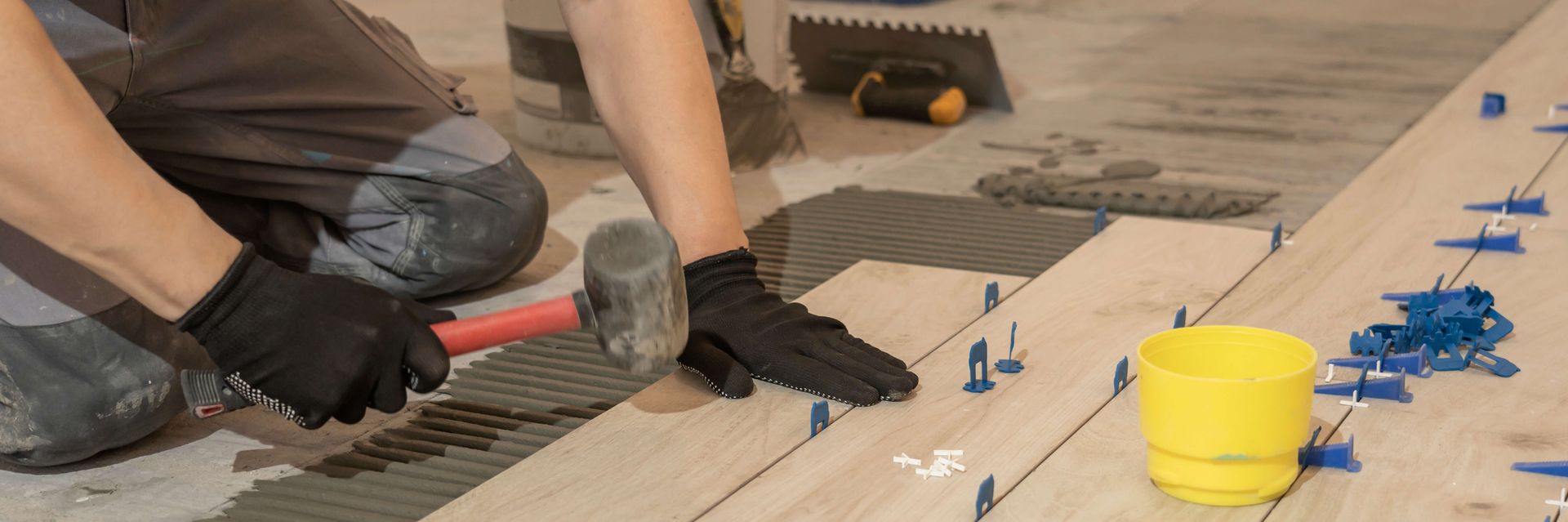 A man is laying tiles on a wooden floor with a hammer.