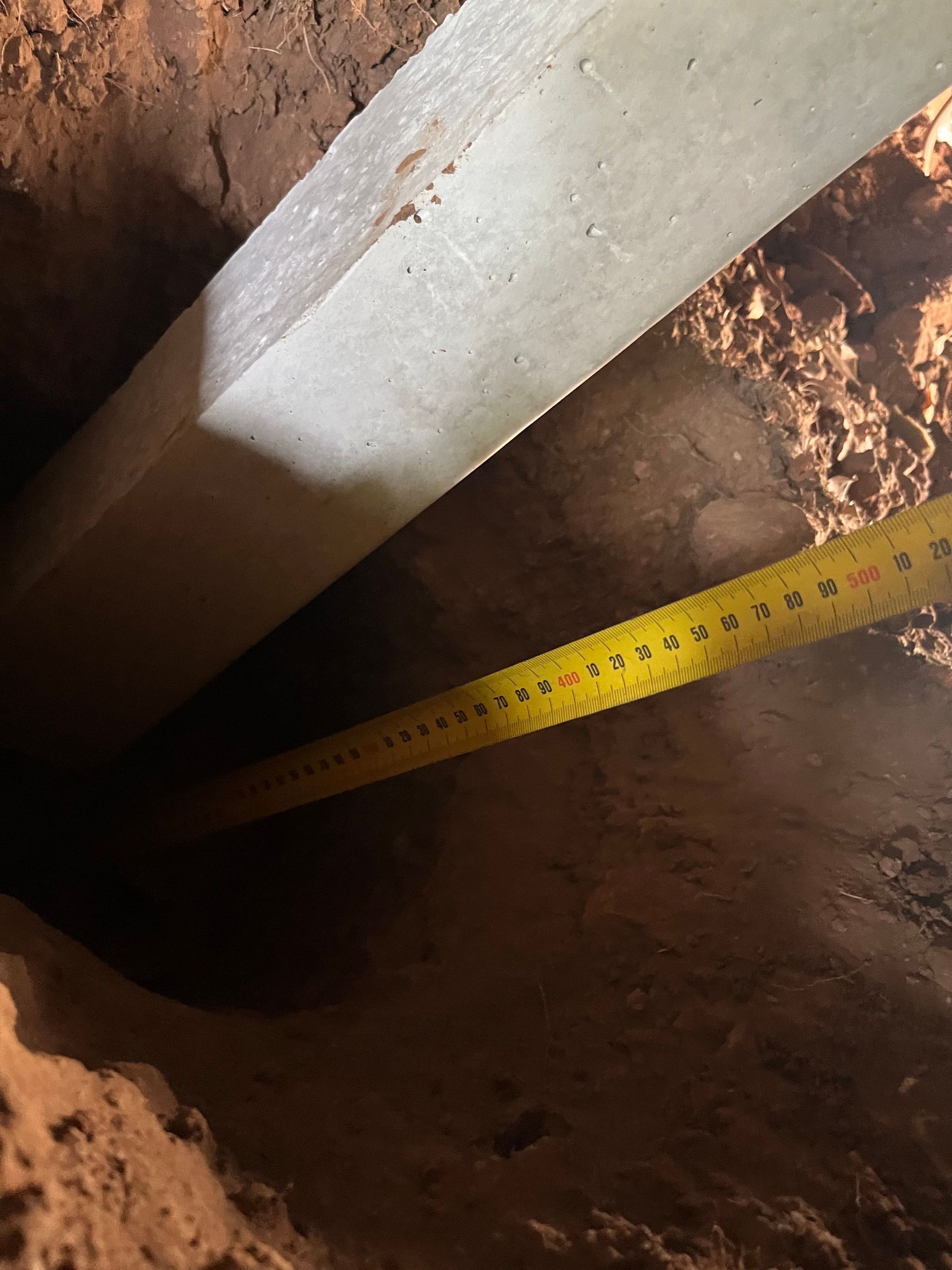 A yellow tape measure is being used to measure a hole in the ground