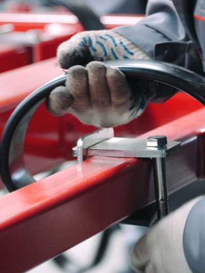 Person in work gloves holding a black handle attached to a red metal frame with a silver bracket.