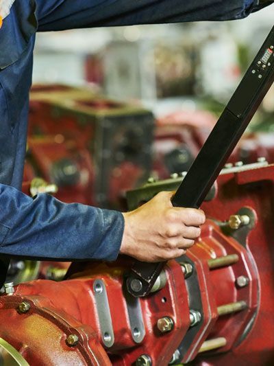 Mechanic in blue overalls operating a lever on a red machine.