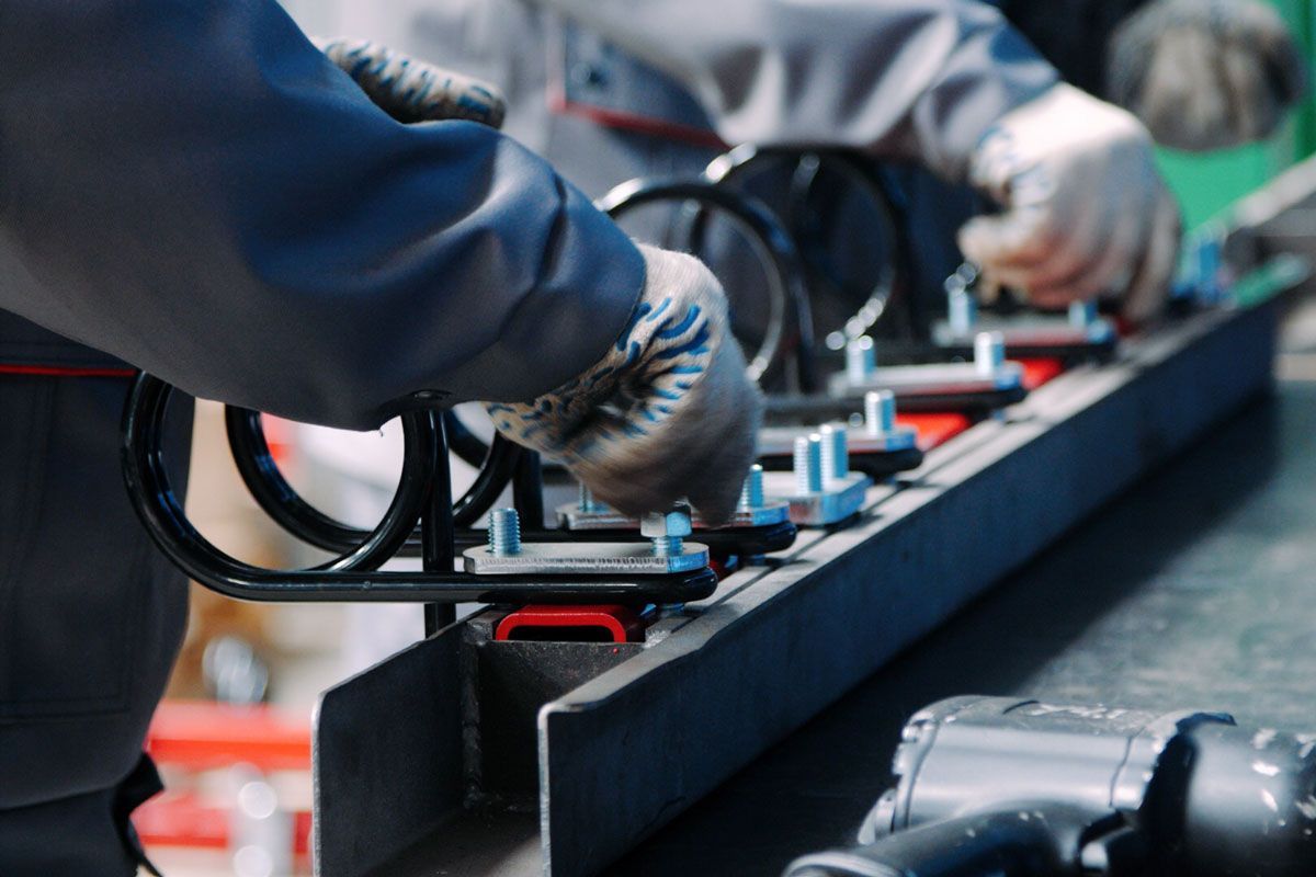 Workers assembling a black suspension system with springs and bolts in a factory setting.