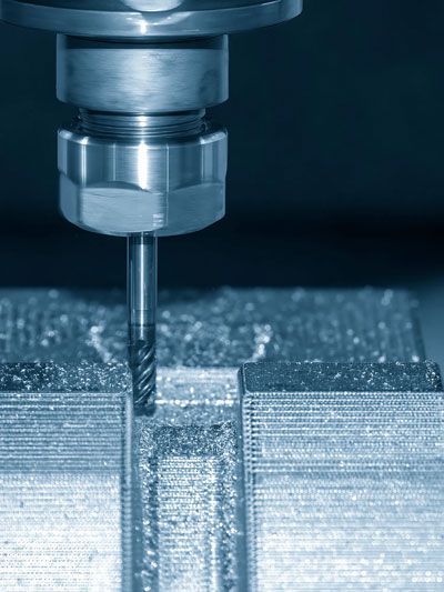 CNC milling machine cutting a groove into a metal block, blue tones.