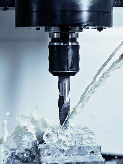CNC machine drilling into metal block, coolant spraying.