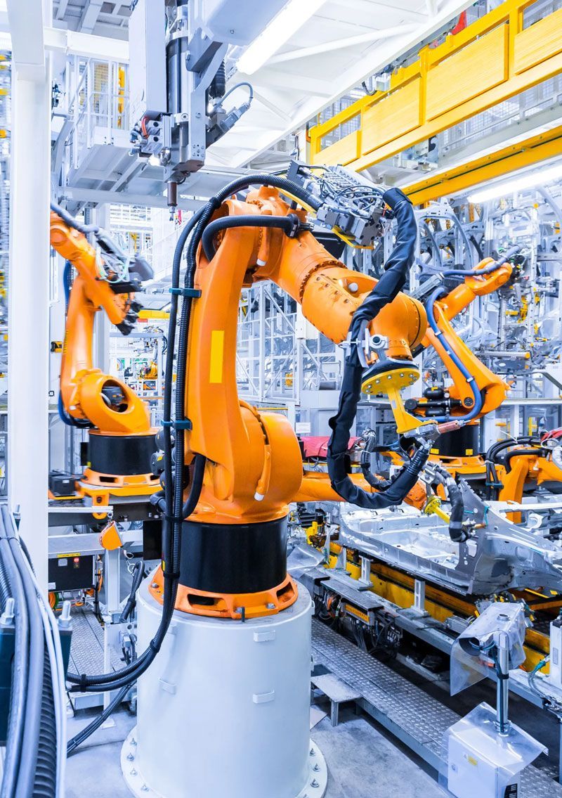 Orange robotic arms in a factory setting, assembling parts.
