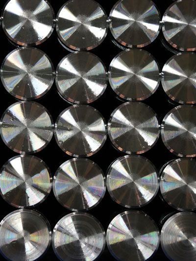 Twenty shiny, circular metallic objects arranged in rows and columns against a black background.