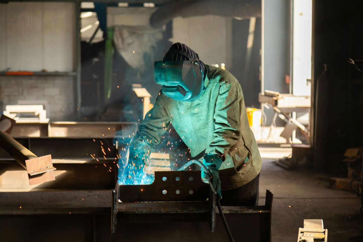 Welder in protective gear welding metal in a workshop, sparks flying.
