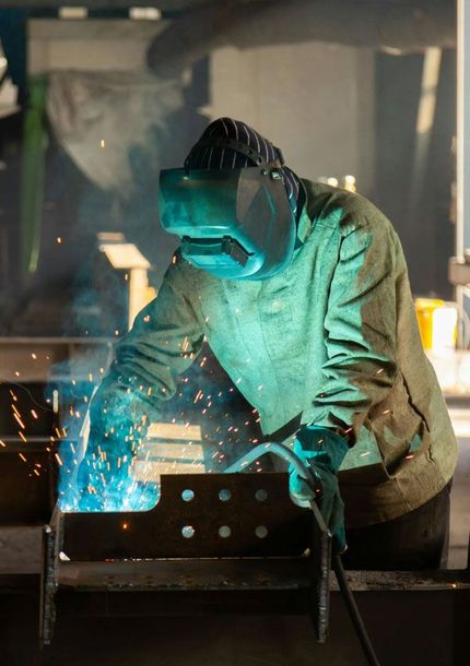 Welder in protective gear, welding metal with bright blue arc and sparks, indoors.