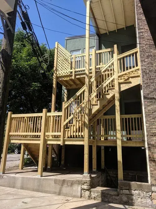 A wooden deck with stairs leading up to the second floor of a building.
