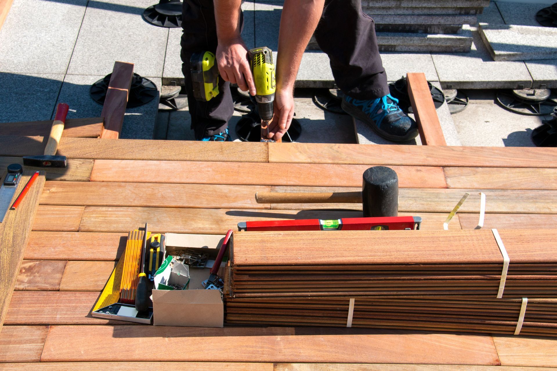 Professional deck contractor using a power drill to install hardwood planks on a rooftop patio. Professional deck contractor using a power drill to install hardwood planks on a rooftop patio.