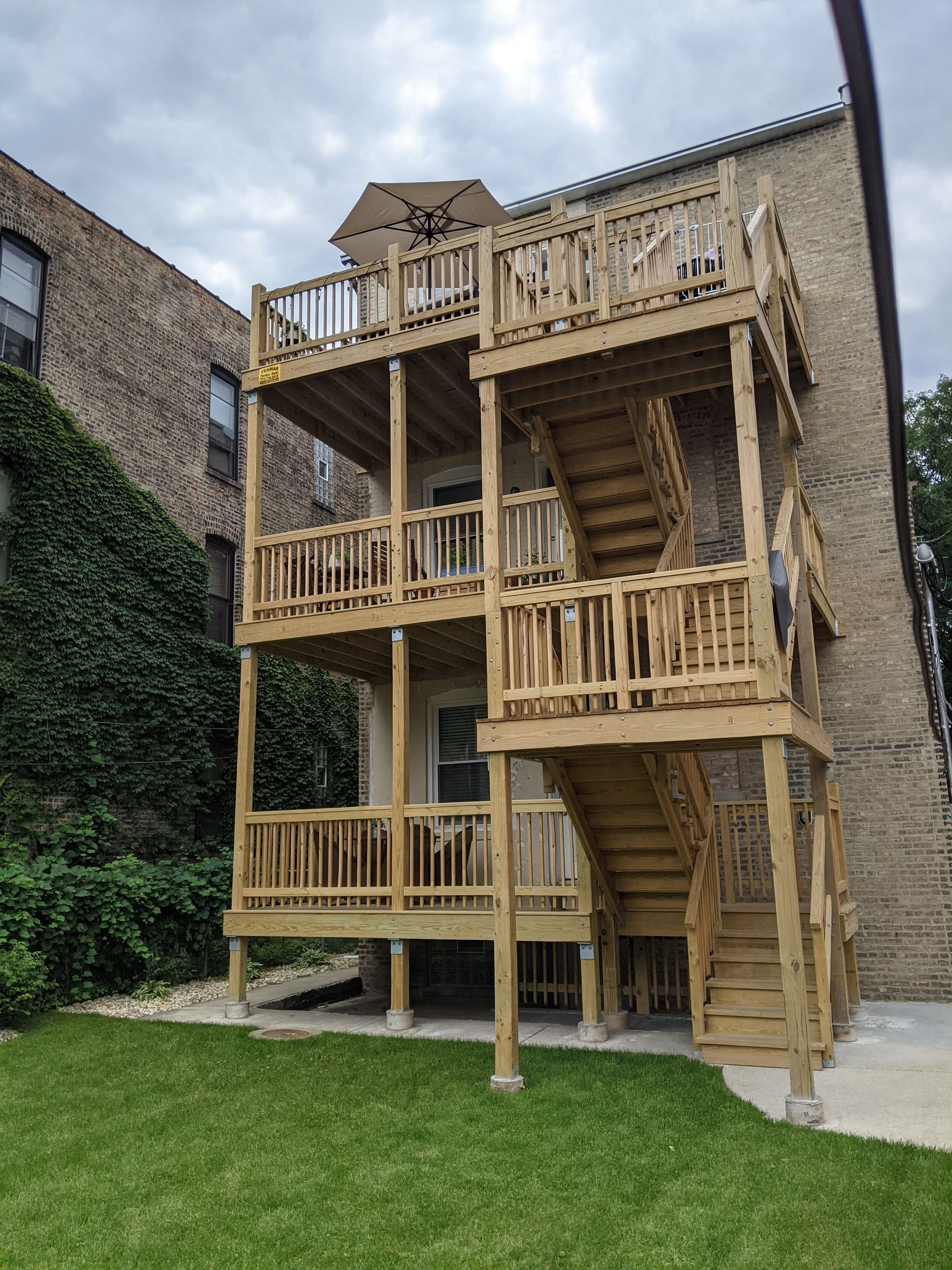 A large wooden deck with stairs is in front of a brick building.