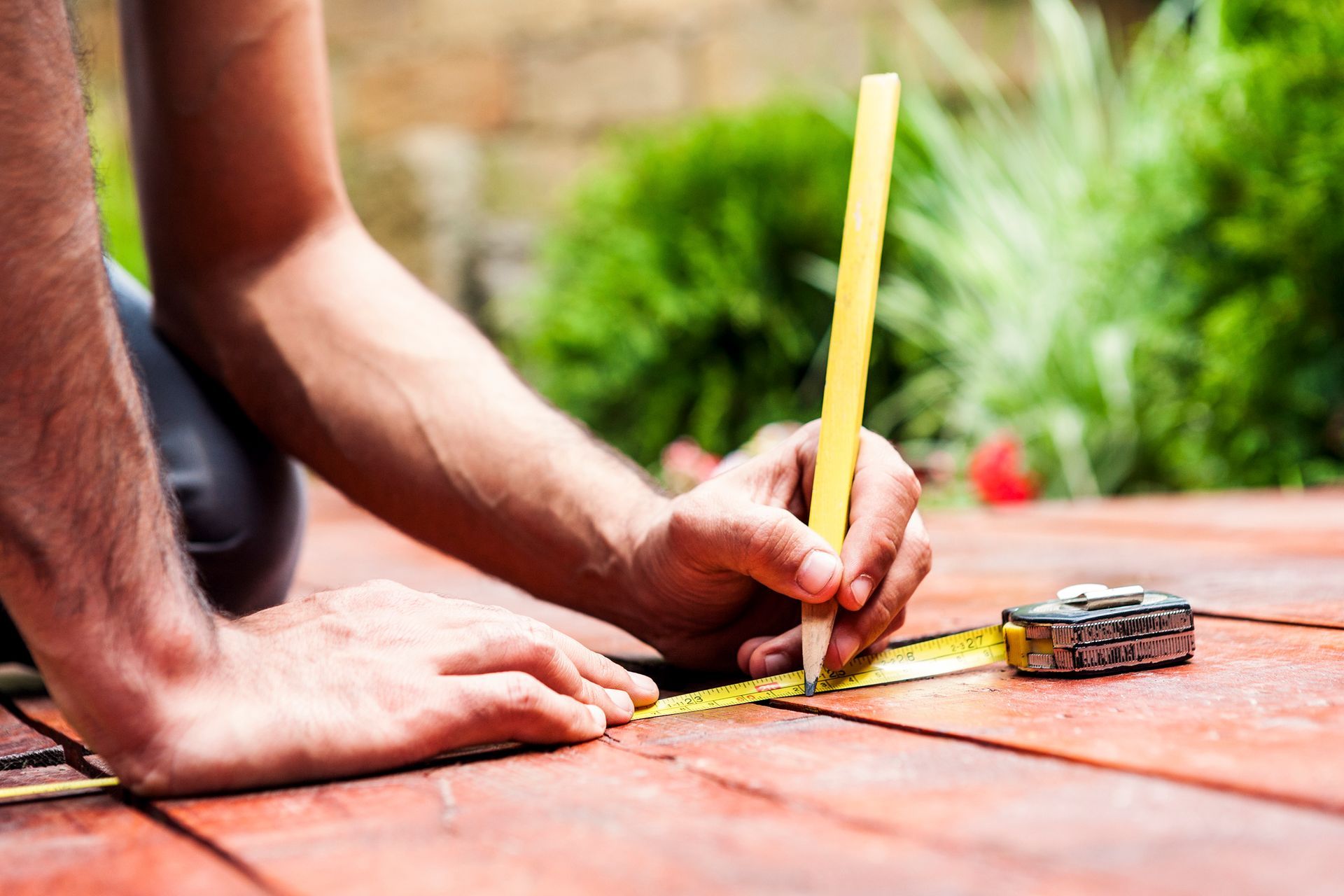 Hands marking wooden deck with tape measure and pencil during outdoor construction project.