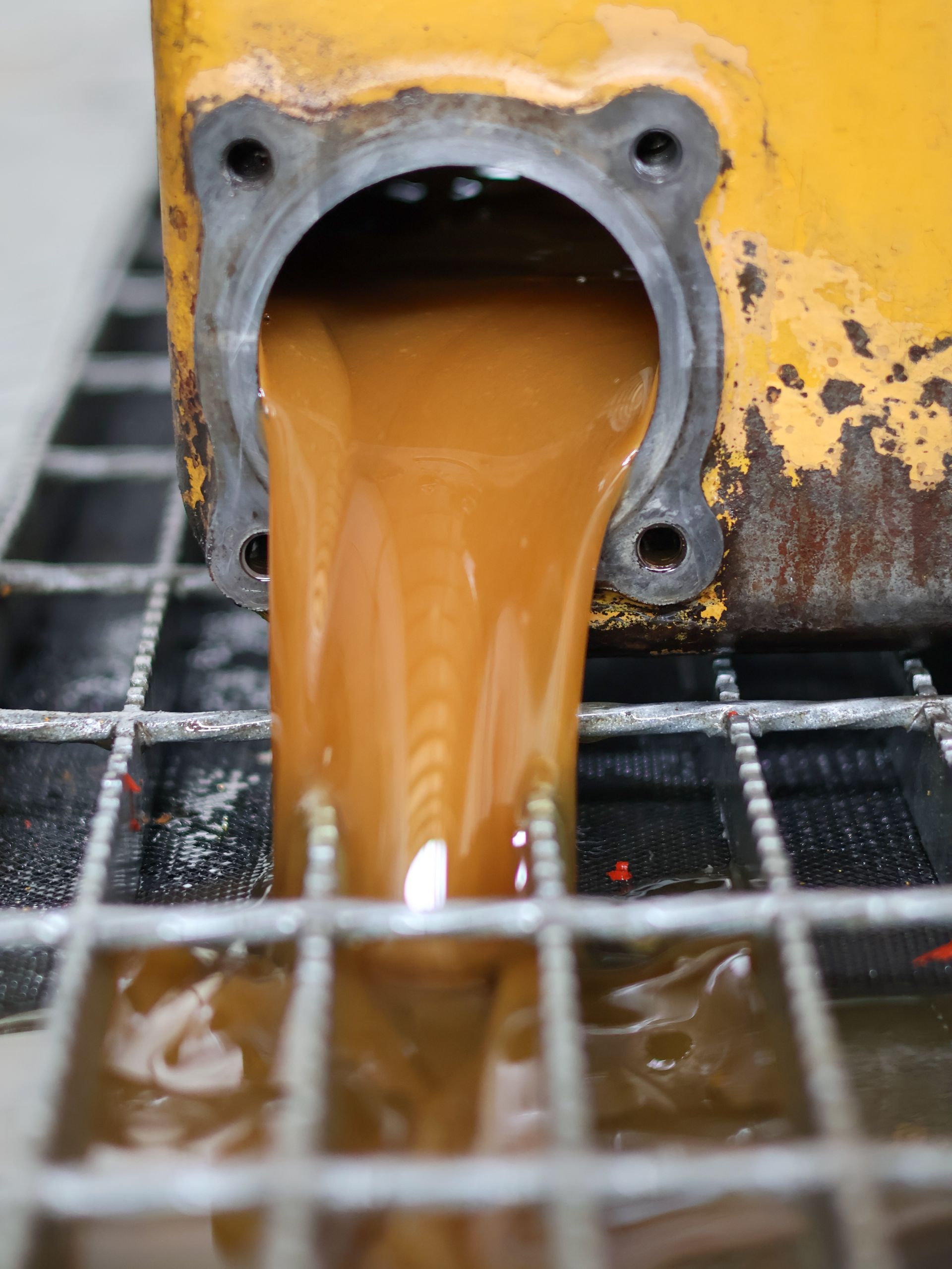 Brown liquid pouring from a yellow metal component onto a metal grate.