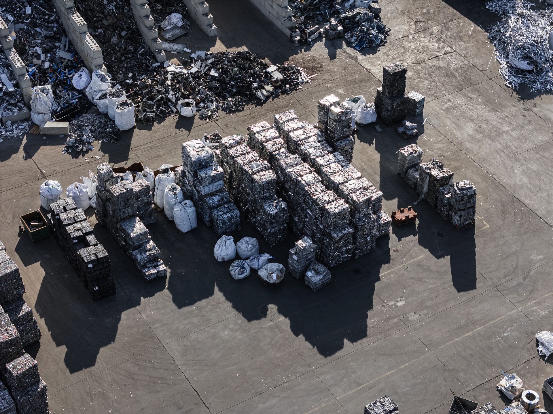Overhead view of a recycling facility. Metal and other materials are sorted and stacked on a gray concrete surface.