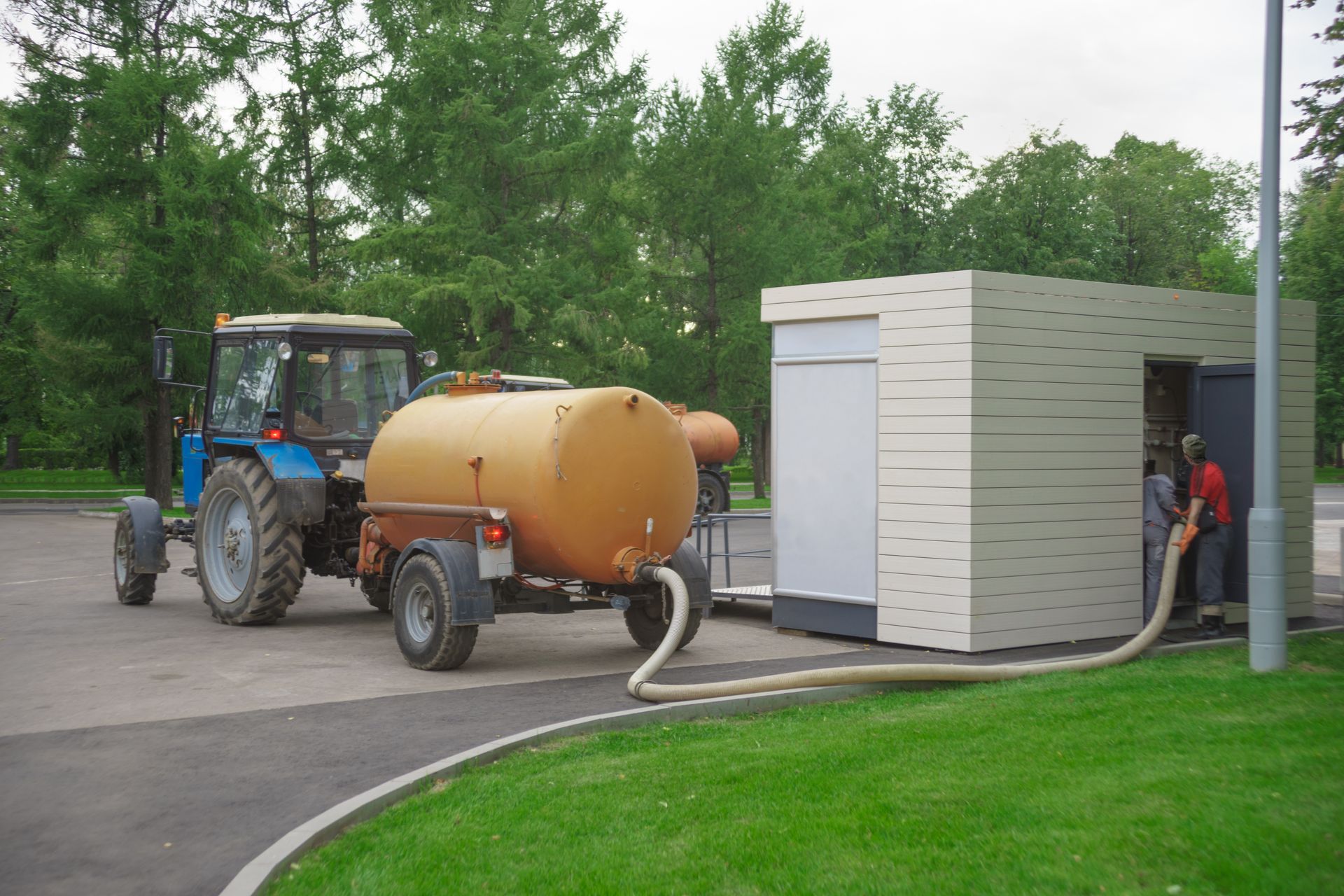 Tractor towing a water tank, connected to a building by a hose. Two people near the building.