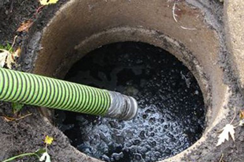 A septic tank being pumped. A large, concrete ring surrounds a dark liquid, a green hose inserted.