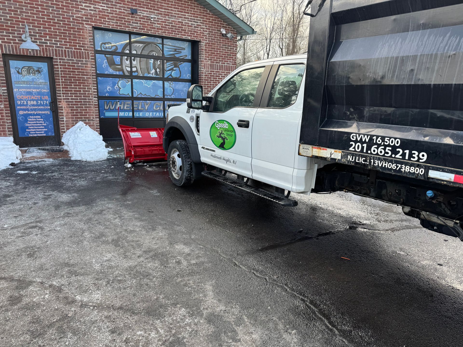 White dump truck with snowplow removing snow in front of a building with a blue door.