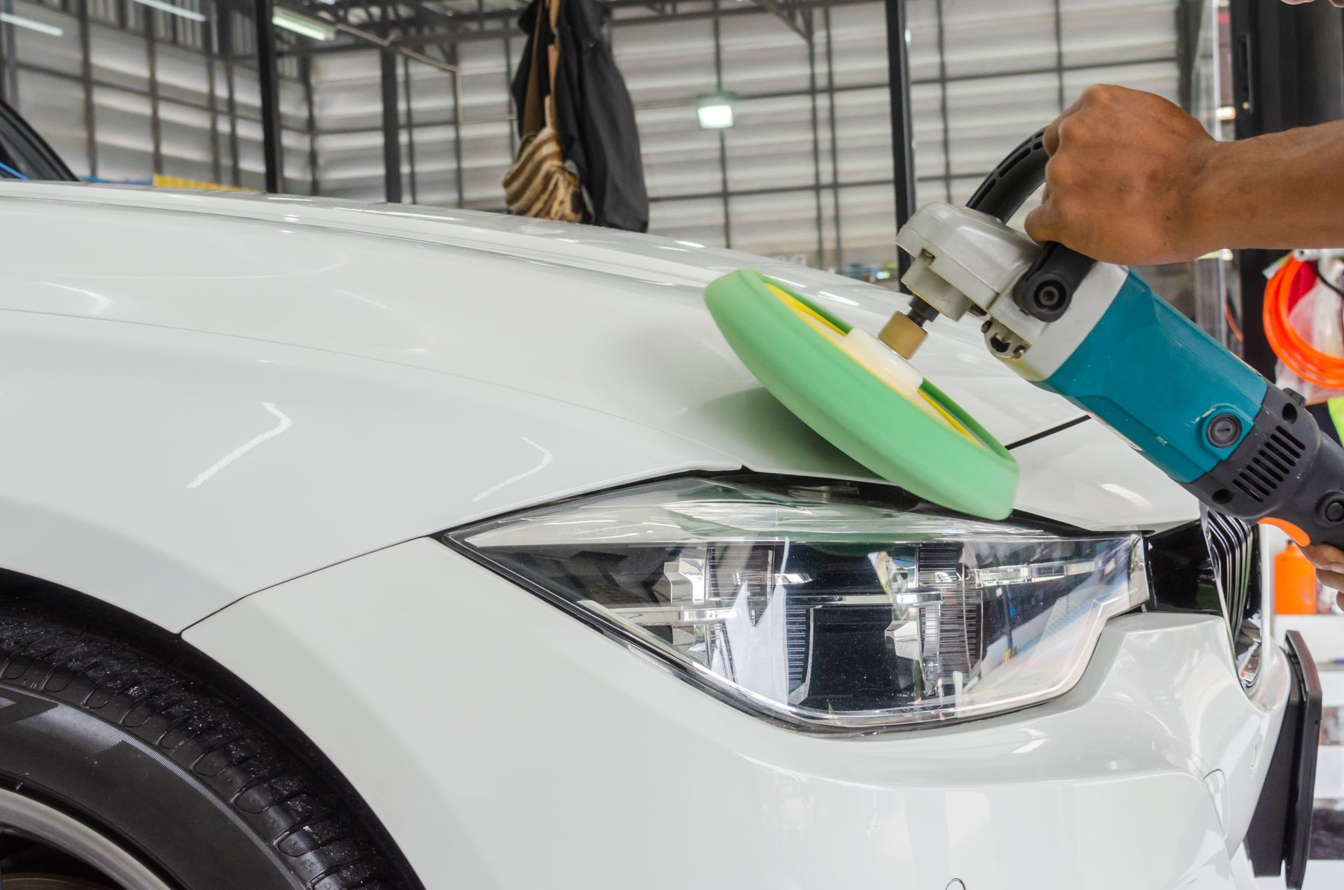 Person using a power polisher on a white car's hood, near the headlight.