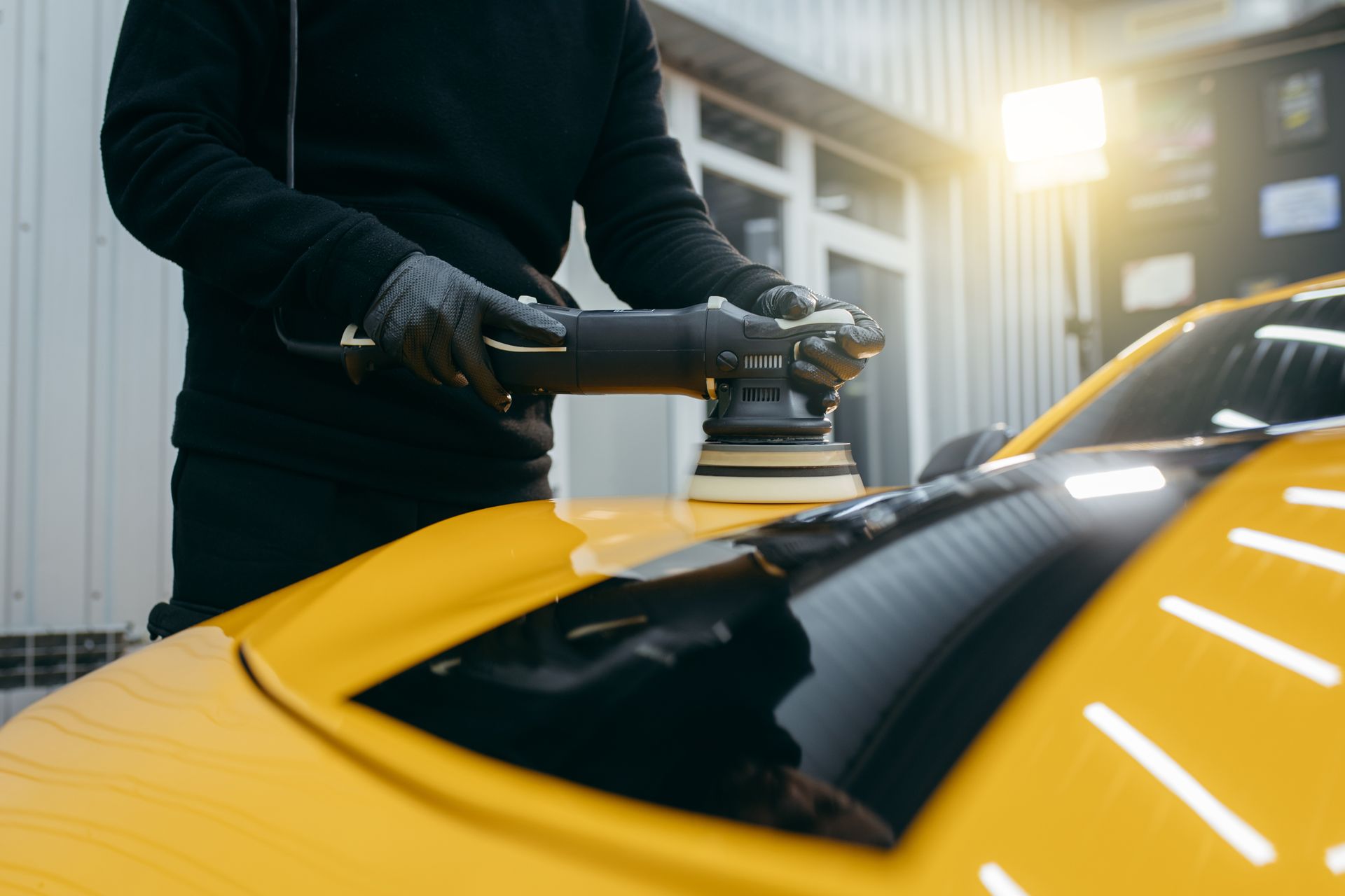 A person polishing a yellow car with a machine in a well-lit garage.